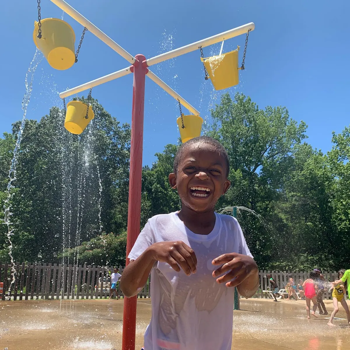 Boy laughing under a splash pad fountain during Bryant Youth Association summer camp in Bryant, AR